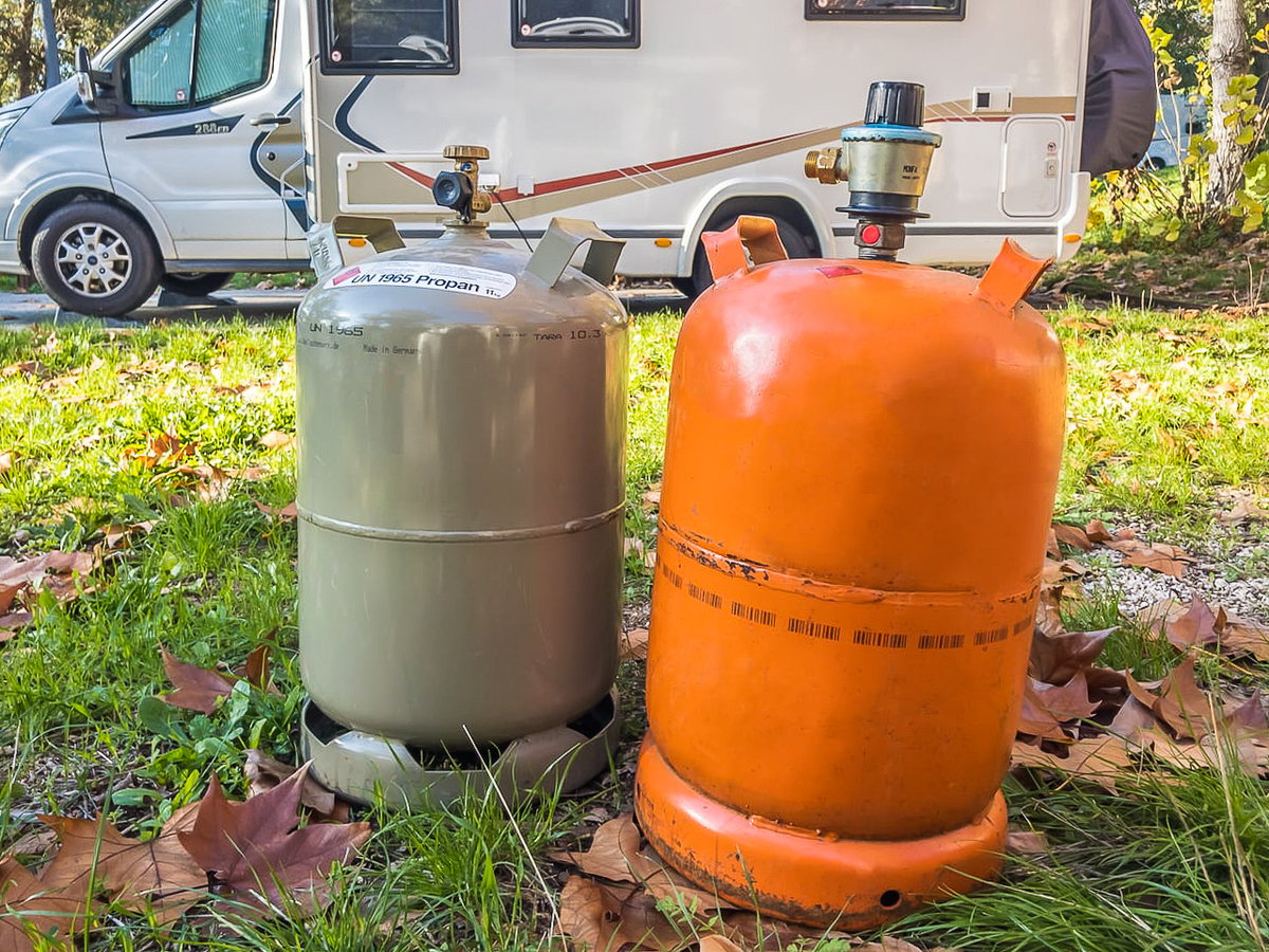 Eine graue und eine orangefarbene Gasflasche beim Camping